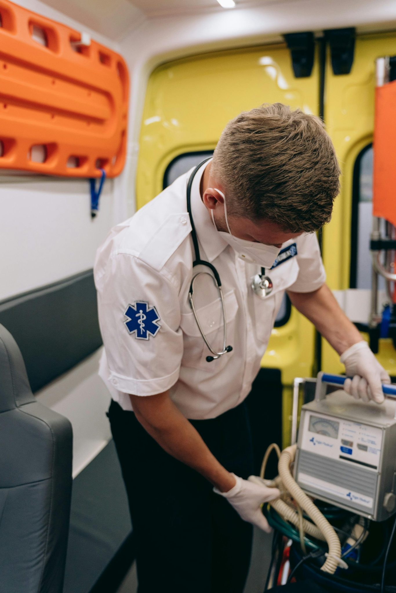 A paramedic wearing a mask operates medical equipment inside an ambulance.